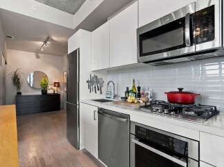 Experience modern urban living in this sleek kitchen featuring stainless steel appliances, including a microwave and dishwasher, complemented by pristine white cabinetry.