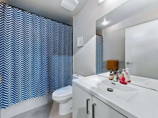 This modern bathroom features a stylish blue and white chevron shower curtain, a sleek white vanity with a large mirror, and a white toilet.