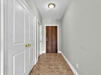 Step into this inviting hallway featuring a warm wooden front door, complemented by elegant white doors and polished tile flooring.