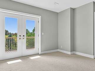 Step out onto your private balcony through elegant French doors, offering a serene view of lush greenery and a clear blue sky.