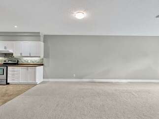 This spacious room features a modern kitchen with white cabinetry, a sleek backsplash, and stainless steel appliances, including a range and oven.