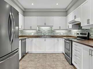 Discover this immaculate kitchen featuring sleek white cabinetry and a stunning glass tile backsplash.