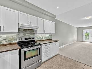 This modern kitchen features sleek white cabinetry and a stylish glass tile backsplash, complemented by a stainless steel range.