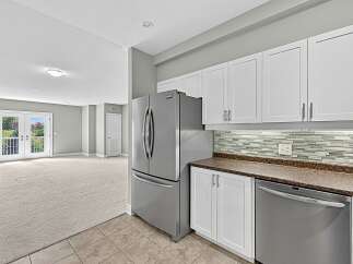 This spacious living area features a modern kitchen with stainless steel appliances, white cabinetry, and a stylish tiled backsplash.