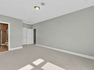 This spacious bedroom features a neutral color palette with light gray walls and a plush, light-colored carpet.