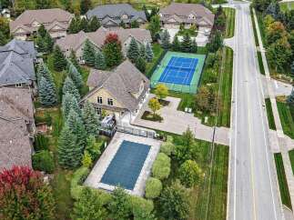 Experience luxury living with this stunning aerial view showcasing a private tennis court and a covered swimming pool, perfect for recreation and relaxation.