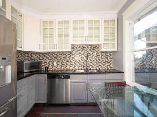This kitchen boasts a sleek stainless steel refrigerator with an ice dispenser, complemented by cream-colored upper cabinets with glass fronts and a mosaic tile backsplash.