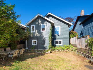 Charming two-story home with classic grey shingle siding and white trim, set against a vibrant blue sky.