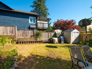 Enjoy outdoor living in this spacious backyard featuring a large wooden deck, a convenient barbecue grill, and two storage sheds for all your gardening tools.