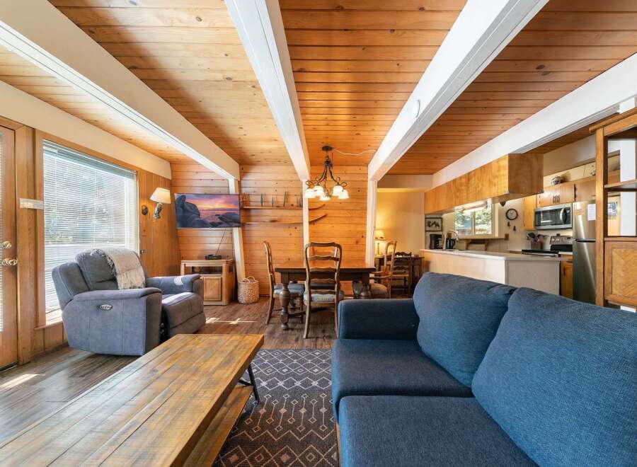 Experience cozy living in this charming cabin featuring a spacious open-concept living area with a rustic wood-paneled ceiling and exposed beams.