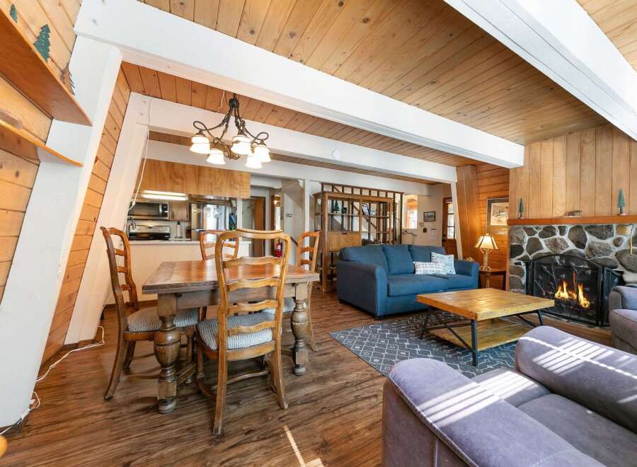 Experience cozy living in this charming A-frame cabin featuring a rustic stone fireplace and a warm, wood-paneled interior.