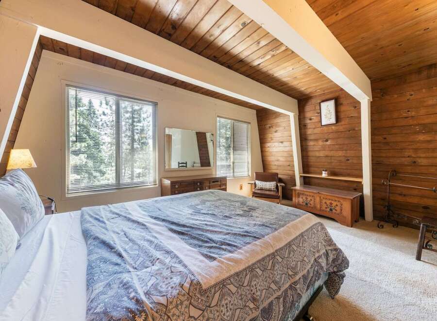 Experience rustic charm in this cozy bedroom, featuring a comfortable bed with a patterned comforter and a large window offering serene views of the surrounding trees.
