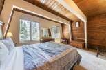 Experience rustic charm in this cozy bedroom, featuring a comfortable bed with a patterned comforter and a large window offering serene views of the surrounding trees.