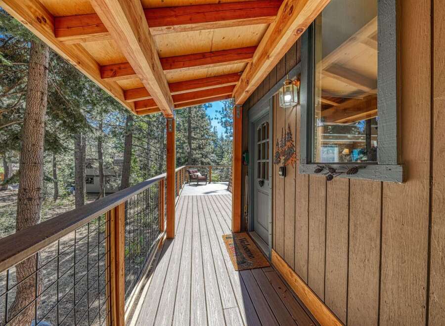 Experience rustic charm with this inviting cabin porch, featuring a spacious wooden deck and a covered roof supported by exposed beams.