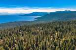 Experience the ultimate mountain retreat with this stunning aerial view of homes nestled within a dense pine forest overlooking a vast, serene lake.
