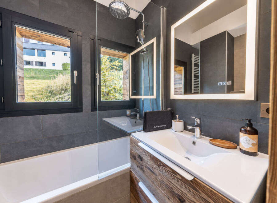 Experience modern comfort in this stylish bathroom, featuring a sleek bathtub and a spacious vanity with a large, illuminated mirror.