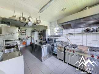 This spacious commercial kitchen is fully equipped for professional use, featuring a large stainless steel island, multiple gas burners, a deep fryer, and ample overhead storage.