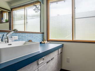 This modern bathroom features a sleek white vessel sink atop a deep blue countertop, complemented by grey cabinetry with minimalist black handles.