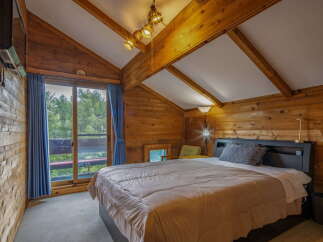 Experience rustic charm in this cozy attic bedroom, featuring warm wood paneling and exposed beams.