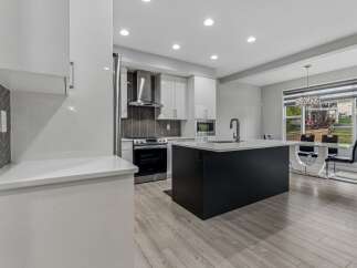 Experience modern living in this stunning kitchen, featuring sleek white cabinetry, a striking dark island with a waterfall countertop, and a herringbone tile backsplash.