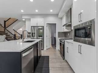 Experience modern living in this stunning kitchen featuring sleek white cabinetry, a spacious island with a waterfall countertop, and high-end stainless steel appliances including a double-door refrigerator and a built-in microwave.