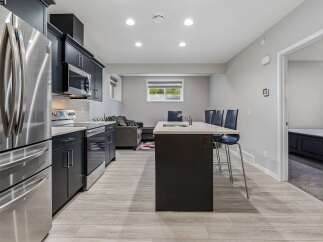 This modern basement suite features a sleek, dark-cabinet kitchen with stainless steel appliances, including a refrigerator, microwave, and stove.