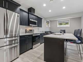 This modern kitchen boasts sleek dark cabinetry, complemented by a stainless steel refrigerator and microwave.