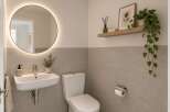 This modern bathroom features a sleek wall-mounted sink with a contemporary faucet, complemented by a round, illuminated mirror that adds a touch of luxury.