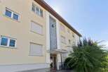 This apartment building features a light yellow facade with multiple windows, some equipped with roller shutters for privacy and light control.