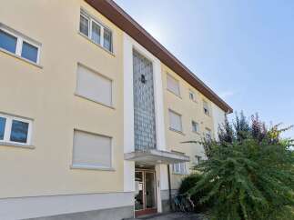 This apartment building features a light yellow facade with multiple windows, some equipped with roller shutters for privacy and light control.