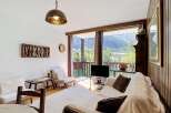Experience breathtaking mountain views from this cozy living room, featuring a comfortable sofa, a rustic wooden coffee table, and a large window overlooking a lush green landscape.