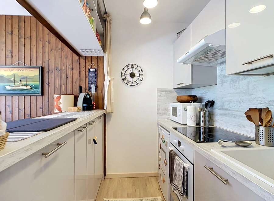 This galley kitchen features a charming wooden accent wall with a framed painting of a boat and a 'CAFFE' sign.