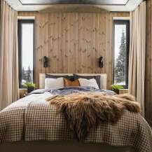Experience cozy luxury in this mountain retreat bedroom, featuring warm wood-paneled walls and a plush king-sized bed adorned with a rustic fur throw.