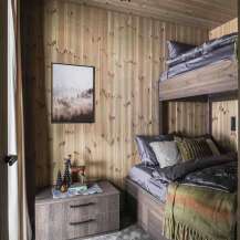 Experience rustic charm in this cozy bedroom featuring a space-saving bunk bed and warm wood-paneled walls.