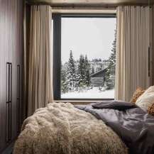 Experience cozy winter living in this charming bedroom, featuring a plush, textured throw blanket and a serene view of a snow-covered forest.