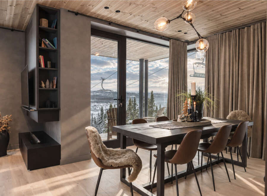 Experience luxury mountain living in this stunning dining area, featuring a sleek dark wood table surrounded by comfortable brown chairs, one adorned with a plush sheepskin throw.
