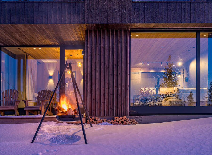 Experience the ultimate cozy retreat in this modern winter cabin, complete with a roaring outdoor fireplace and comfortable Adirondack chairs.