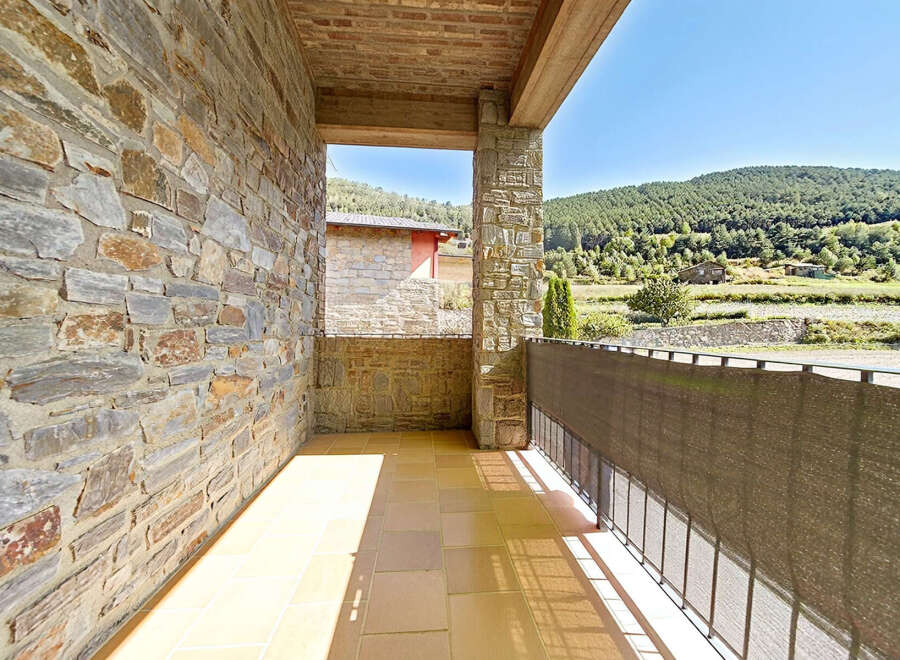 Enjoy the serene mountain views from this charming balcony, featuring a rustic stone wall and a tiled floor.