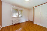 This empty room features a large window with blinds, a modern horizontal radiator, and a built-in sliding door wardrobe.