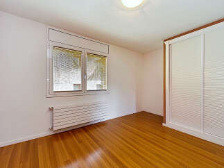 This empty room features a large window with blinds, a modern horizontal radiator, and a built-in sliding door wardrobe.