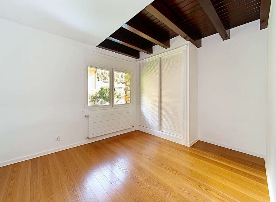 This empty room features a beautiful wooden floor that reflects the natural light streaming in from the large window.
