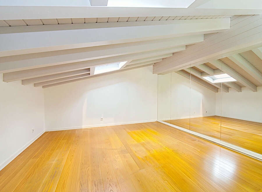 This spacious attic room boasts a stunning vaulted ceiling with exposed white beams, creating an airy and open atmosphere.