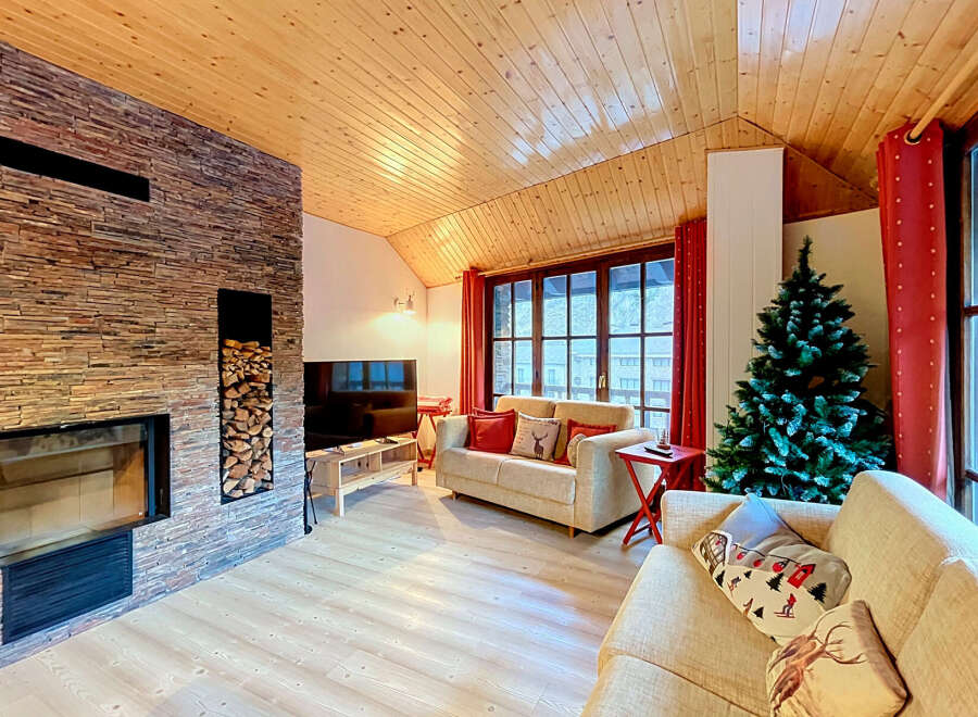 Experience cozy mountain living in this charming living room, featuring a striking stone fireplace and a warm, wood-paneled ceiling.