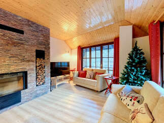 Experience cozy mountain living in this charming living room, featuring a striking stone fireplace and a warm, wood-paneled ceiling.