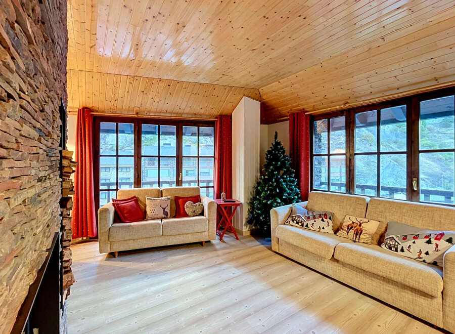 Experience cozy living in this charming mountain retreat, featuring a stunning stone fireplace and a warm, wood-paneled ceiling.