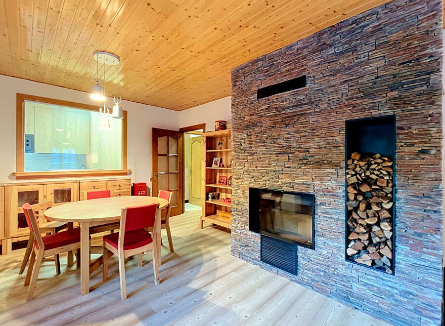 Experience cozy living in this charming dining area, featuring a rustic stone fireplace and a warm wooden ceiling.