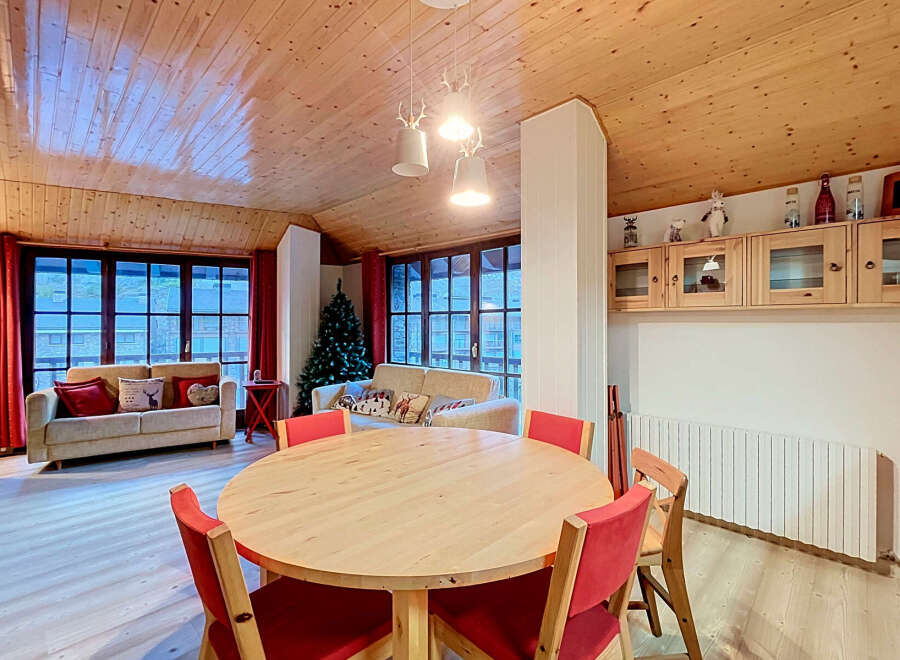 Experience cozy living in this charming mountain retreat, featuring a spacious dining area with a round wooden table and vibrant red chairs, perfect for family gatherings.
