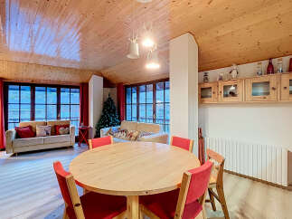 Experience cozy living in this charming mountain retreat, featuring a spacious dining area with a round wooden table and vibrant red chairs, perfect for family gatherings.