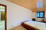 This charming bedroom features a comfortable wooden bed with a patterned mattress, set against a backdrop of white walls and a warm, slatted wooden ceiling.