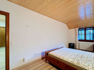 This charming bedroom features a comfortable wooden bed with a patterned mattress, set against a backdrop of white walls and a warm, slatted wooden ceiling.